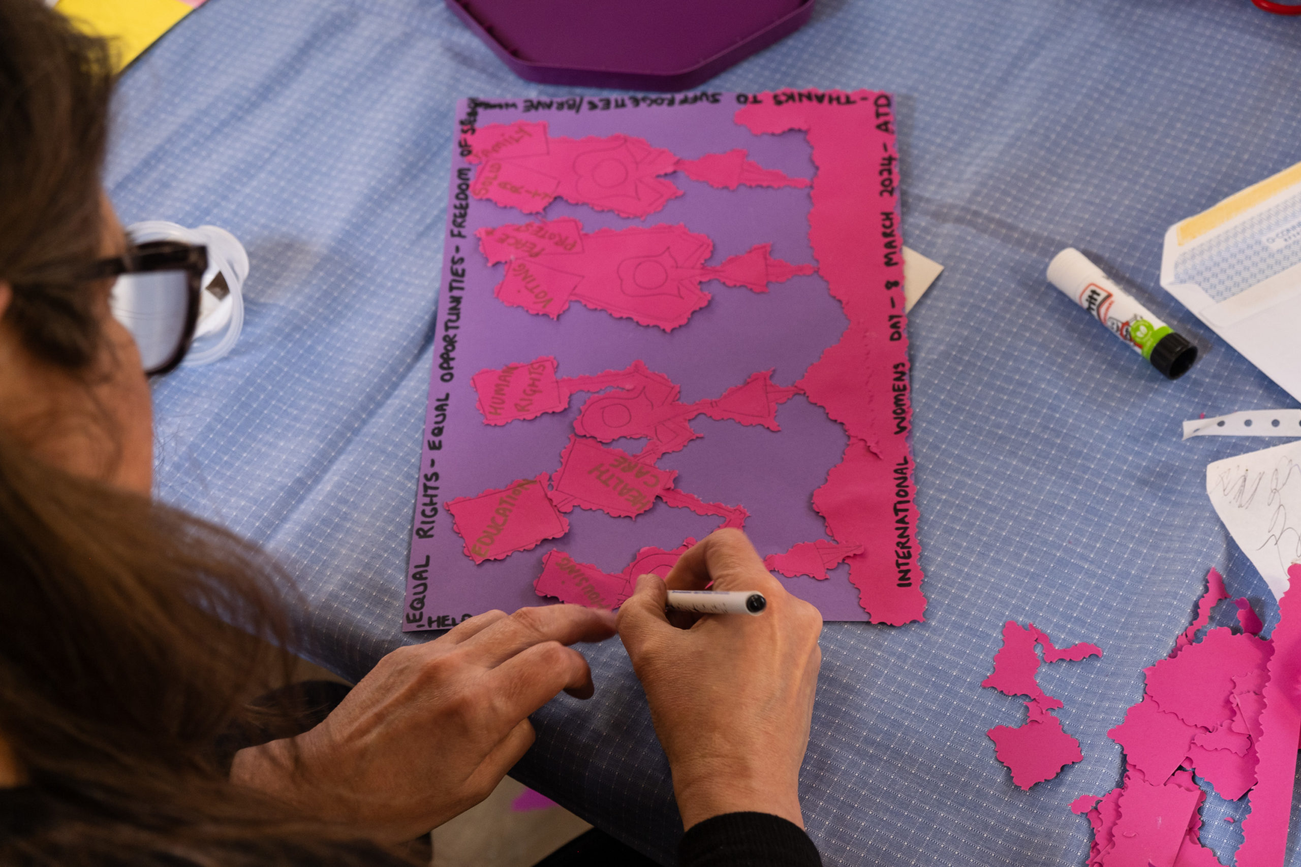 A woman is creating a pink and purple collage representing the suffragettes, at a women's day creative workshop.