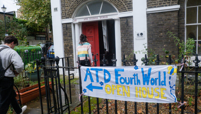 Two people are entering a house, and a banner pointing to the door reads: "ATD Fourth World, Openb House". There are balloons near the banner and bunting above the door.