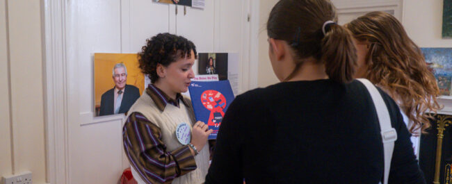 A woman is holding a book, and two women are listening to her and looking at the book.
