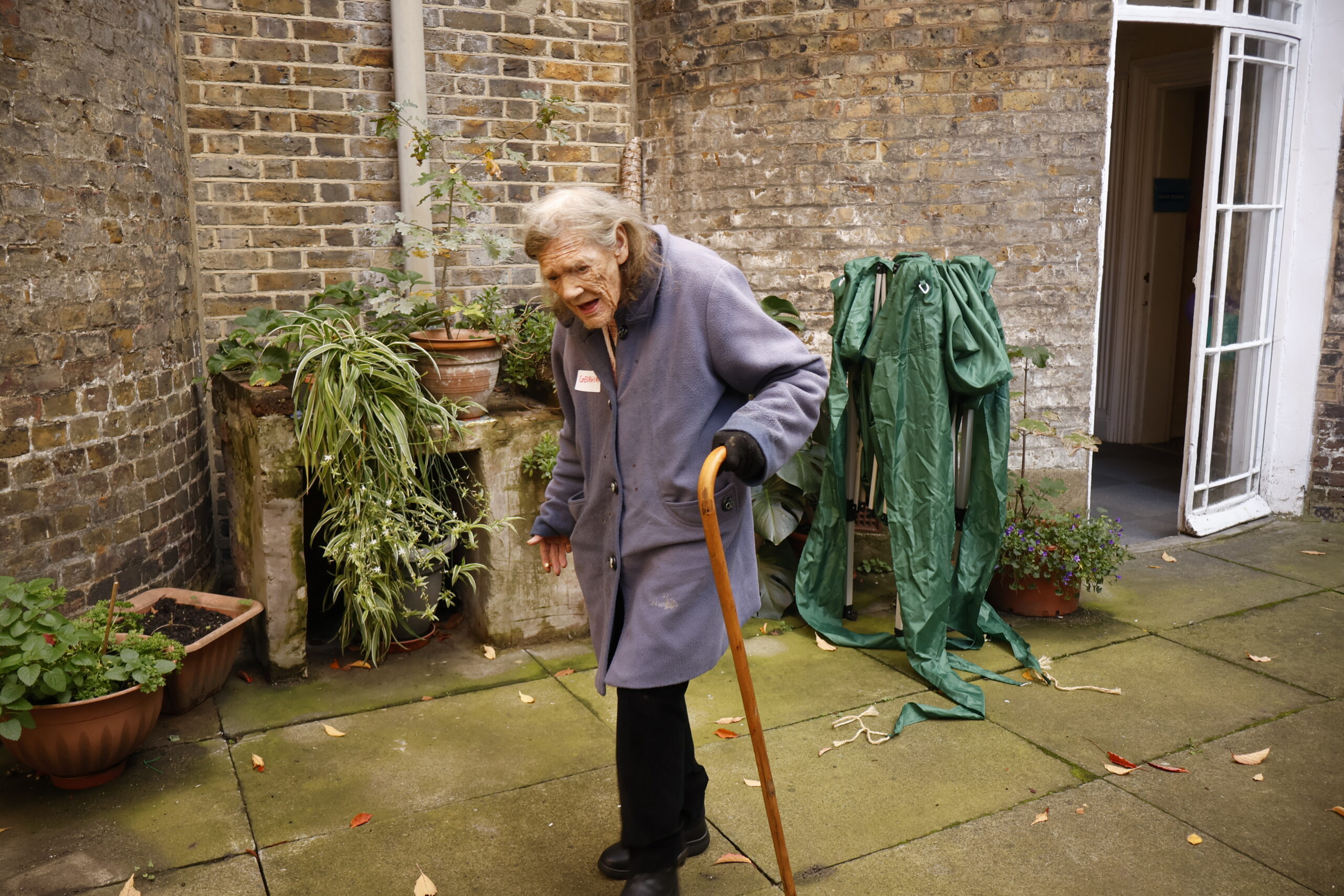 A woman with a cane is walking in the middle of a courtyard.